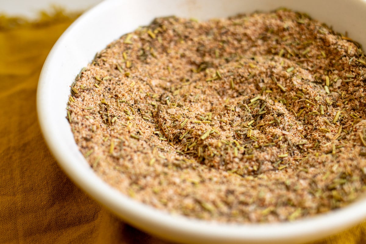 a white bowl full of colorful spices that make up turkey seasoning - like rosemary, sage, thyme, pepper, garlic, salt.