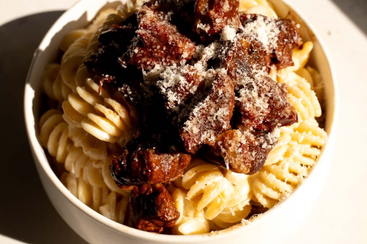 a bowl of creamy parmesan noodles with crockpot slow cooker garlic steak bites on top.