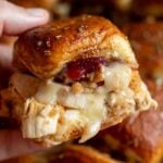 a hand holding a thanksgiving inspired turkey cranberry slider with brie cheese dripping from it and stuffing coming out.