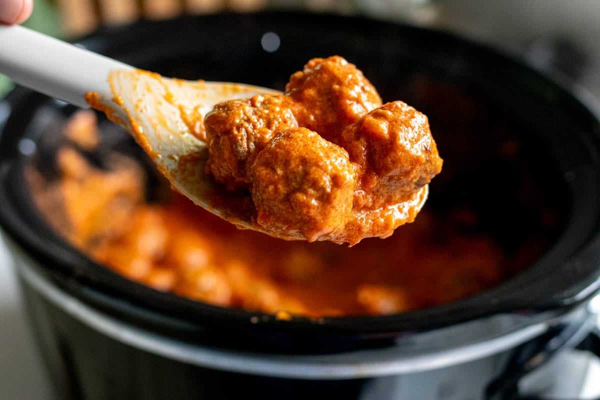 a wooden spoon holding a few creamy tomato crockpot meatballs.