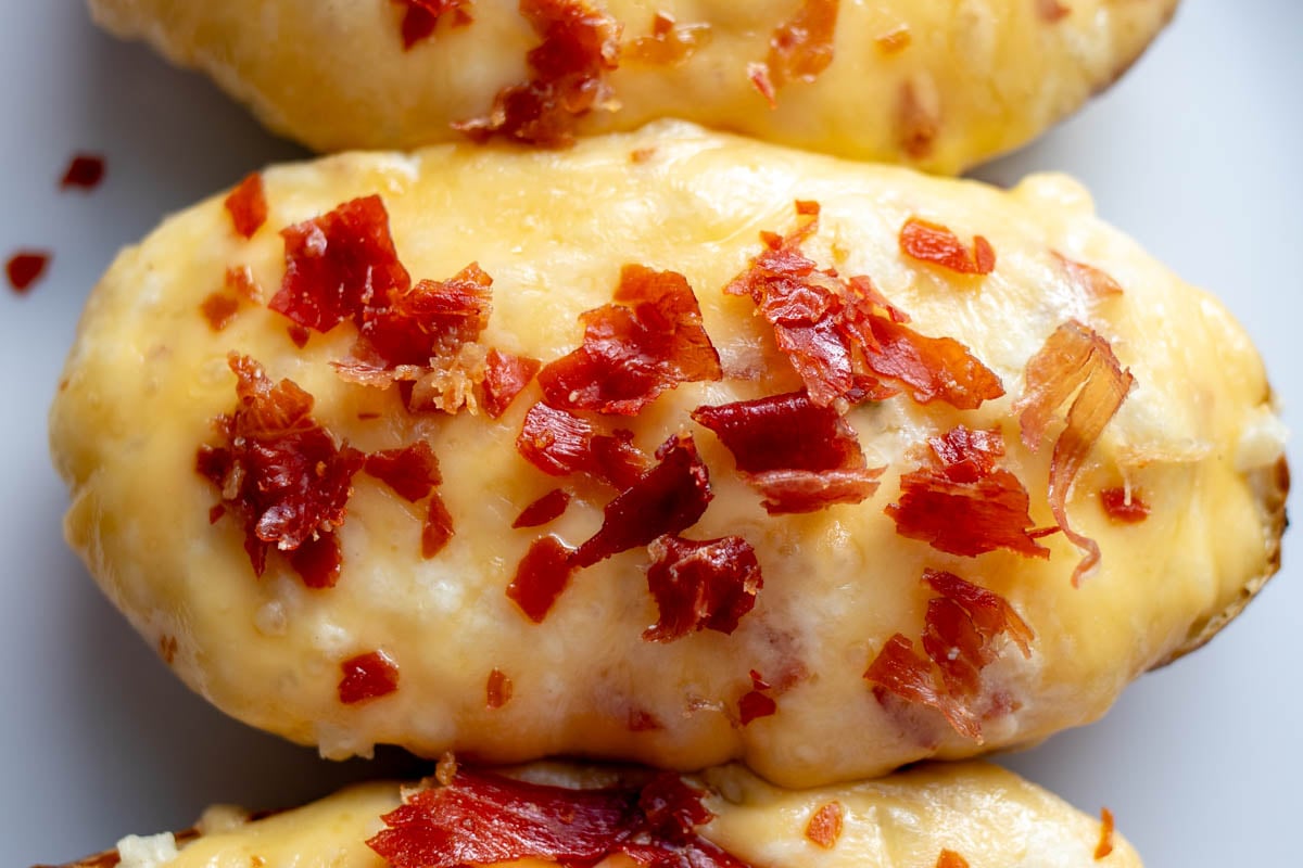 a close up of a singular twice baked potato on a white surface with crispy bits of crumbled prosciutto and melty cheesy on top.