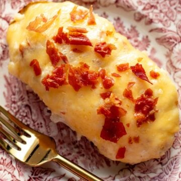 a single cheesy twice baked stuffed potato with crispy bits of prosciutto on top with a gold fork and pink and white plate.