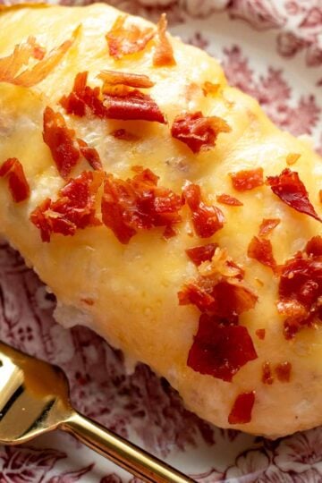 a single cheesy twice baked stuffed potato with crispy bits of prosciutto on top with a gold fork and pink and white plate.