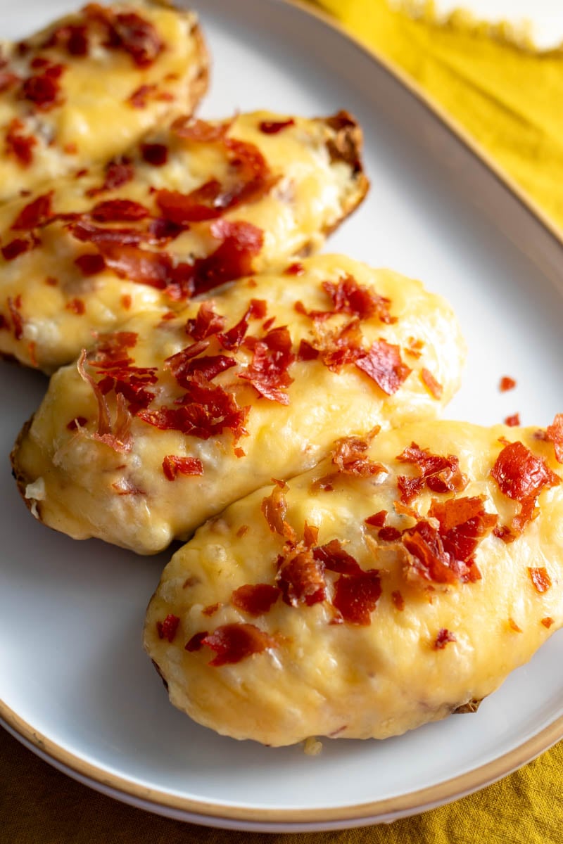 a white serving platter topped with cheesy twice baked stuffed potatoes with crispy red bits of prosciutto on top.