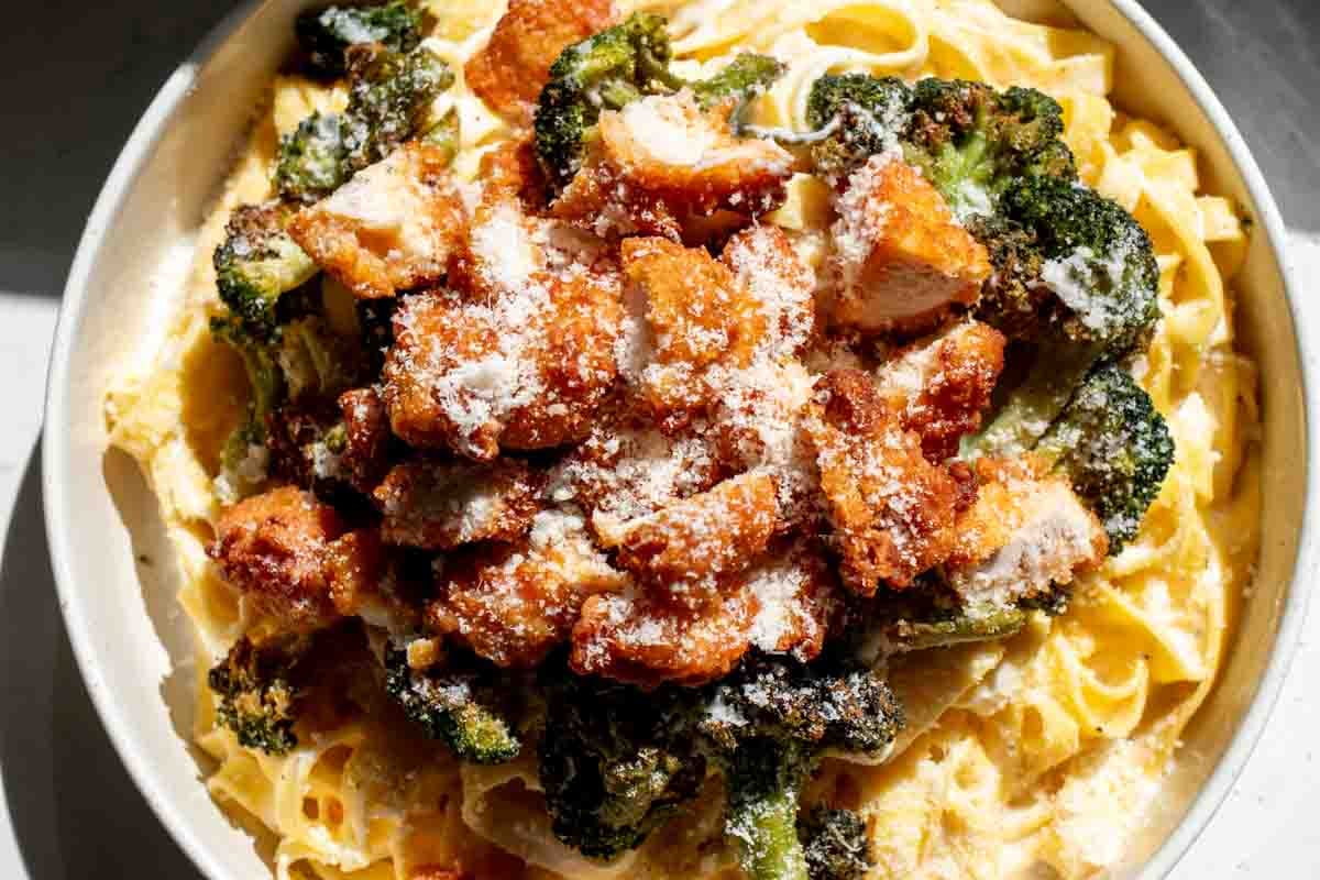 an overhead view of a bowl of chicken broccoli fettuccine alfredo with parmesan on top.