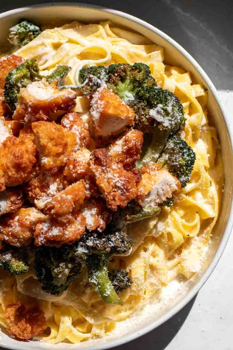 an overhead view of a bowl of chicken broccoli fettuccine alfredo with parmesan on top.