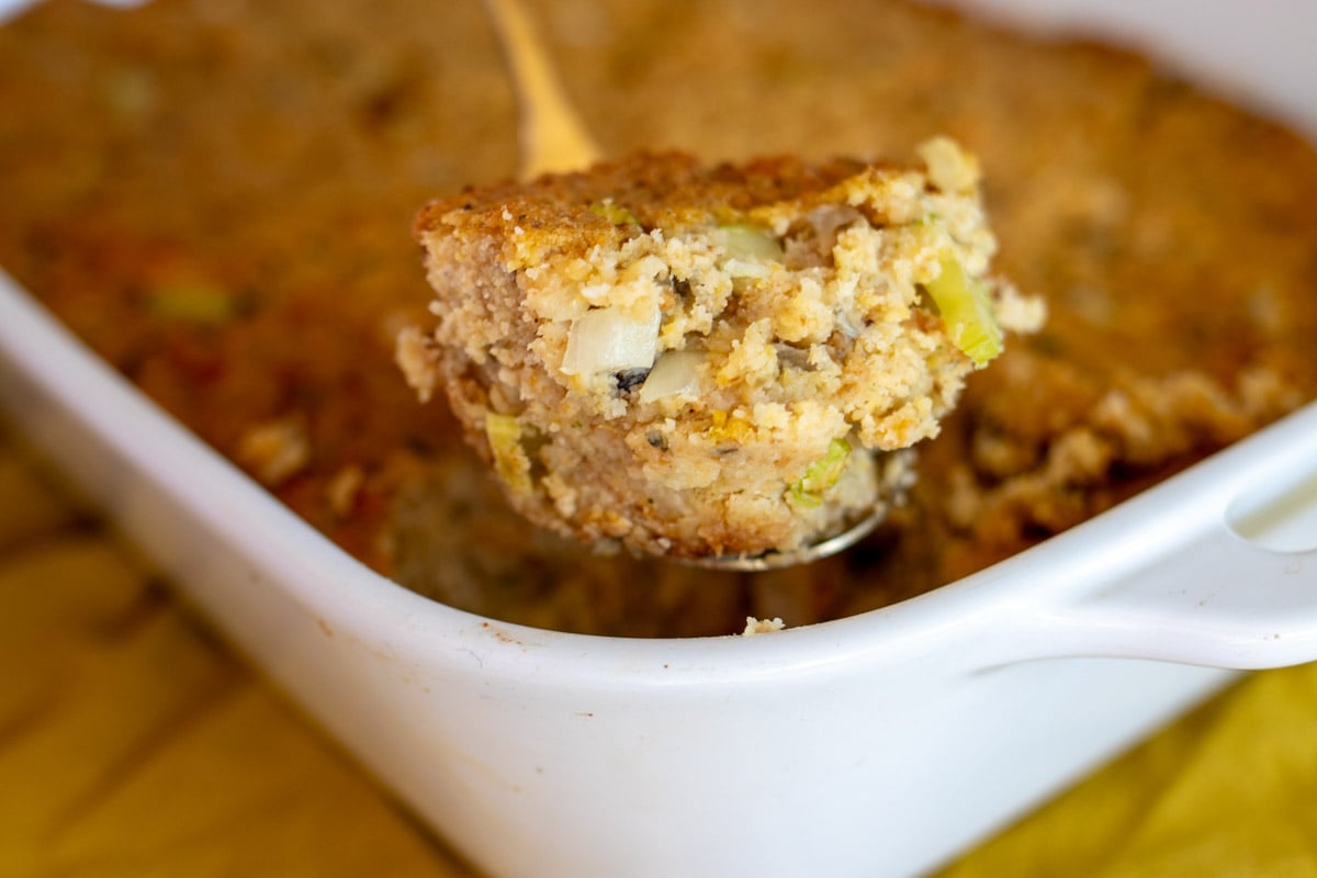 a scoop of oyster dressing in a gold spoon over the top of the baking dish.