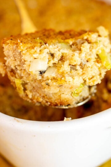 a scoop of oyster dressing in a gold spoon over the top of the baking dish.