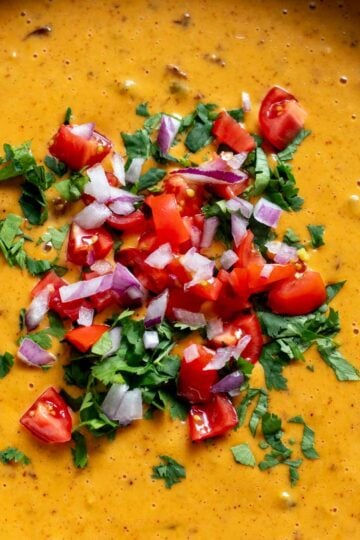 a crockpot bowl full of bright orange cheese dip with colorful cilantro, tomato and onion on top.