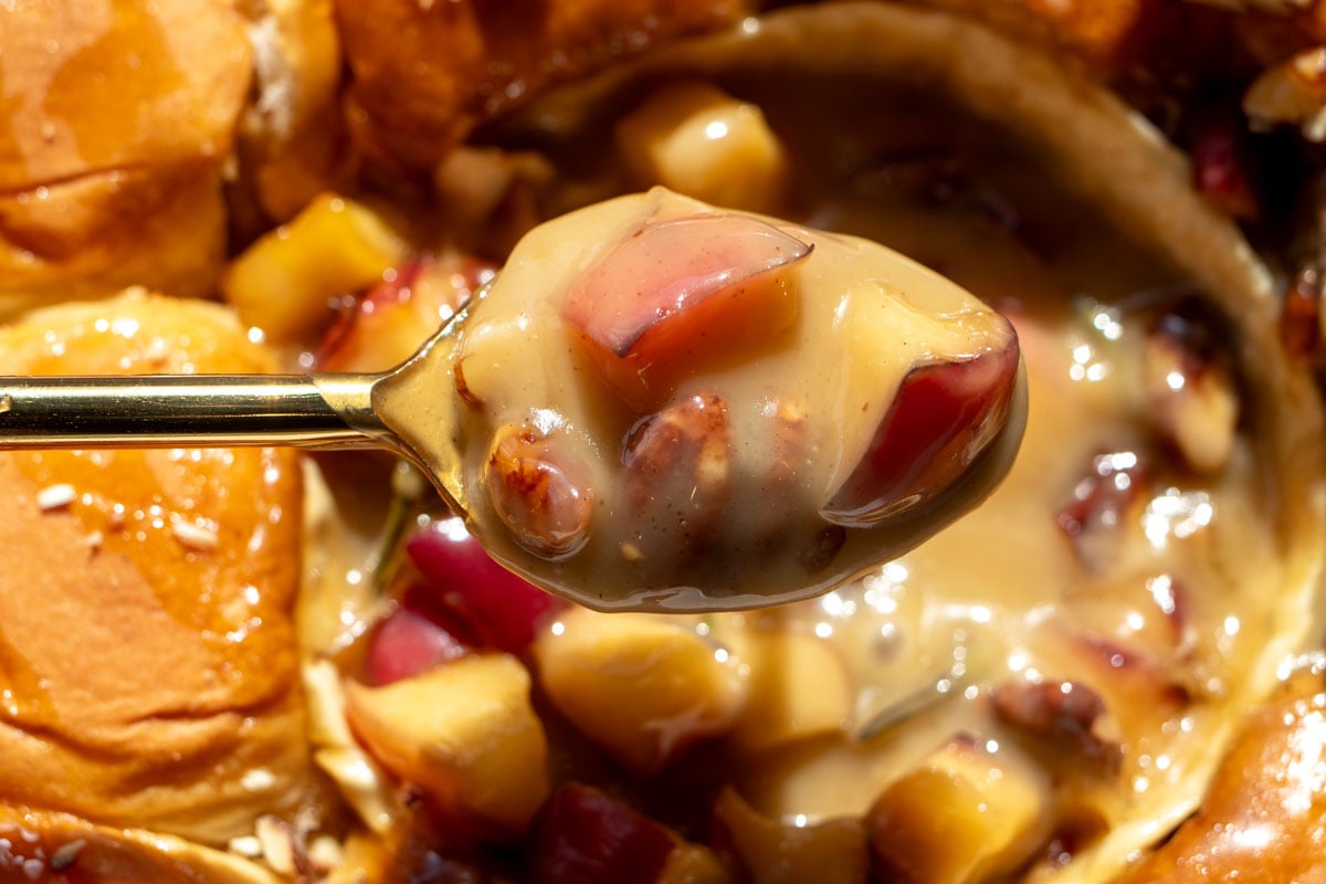 a spoon scooping up some melty brie cheese and caramelized apples.