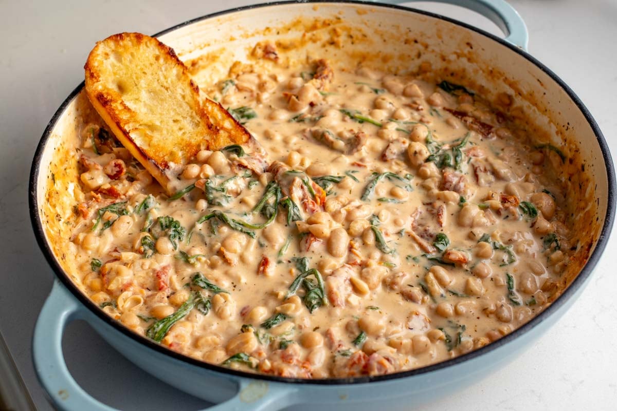 a big pot of marry me beans in a creamy tuscan sauce with sun dried tomatoes spinach and crusty bread.