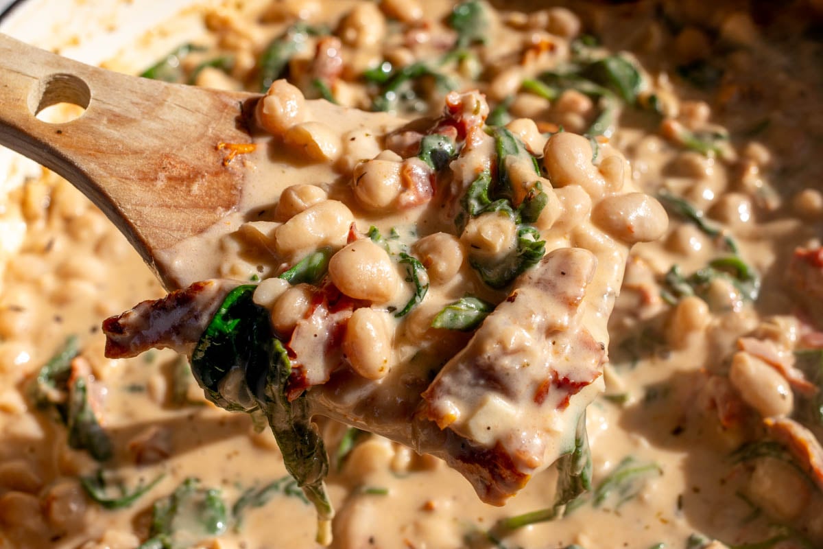 a big wooden spoon holding a scoop of marry me beans.