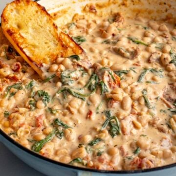 a big pot of marry me beans in a creamy tuscan sauce with sun dried tomatoes spinach and crusty bread.