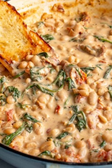 a big pot of marry me beans in a creamy tuscan sauce with sun dried tomatoes spinach and crusty bread.