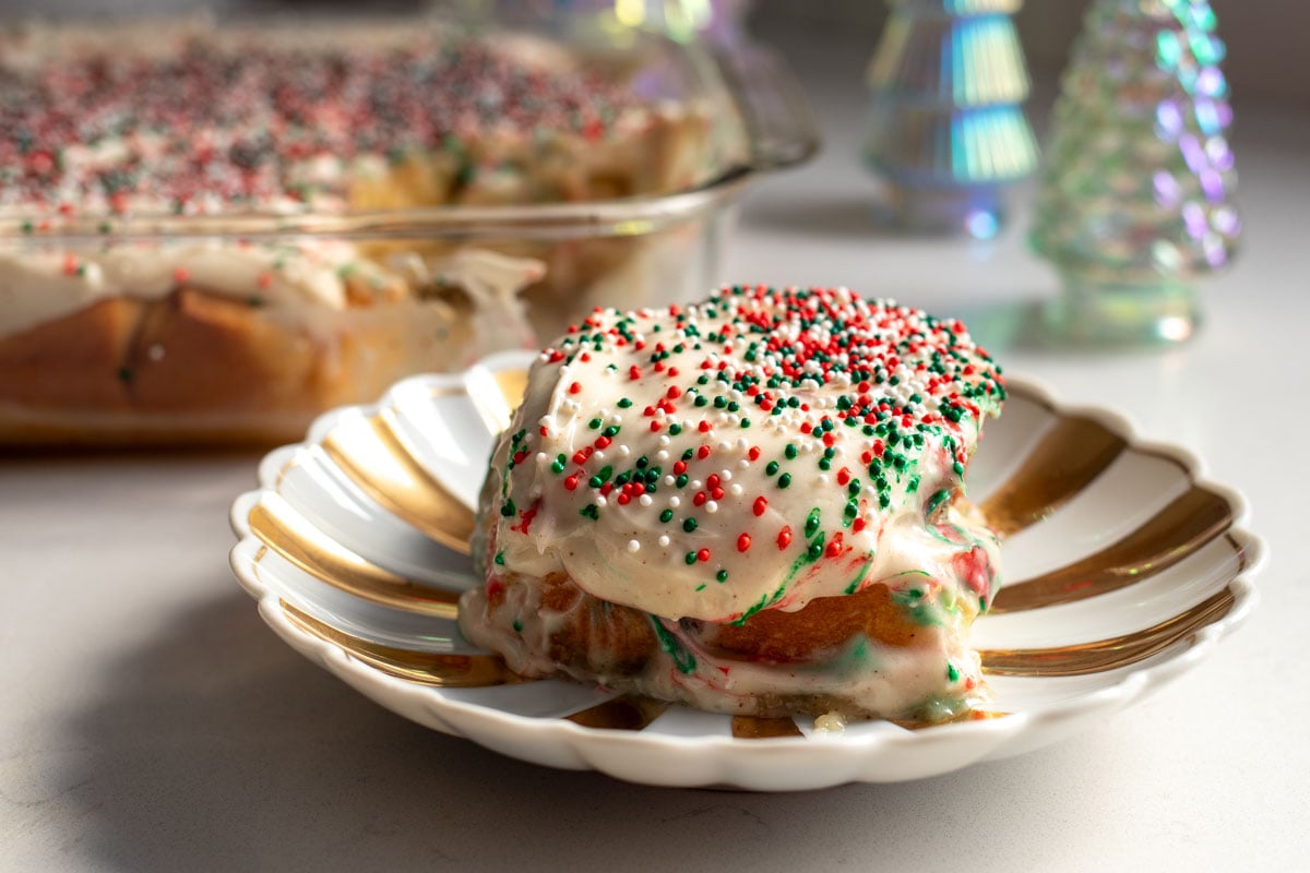 sugar cookie cinnamon rolls sitting on a white table with christmas decor in the background. 