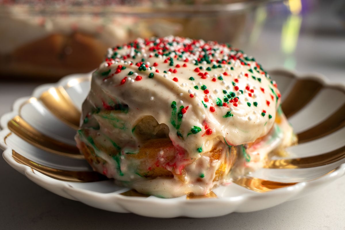 a close up look at these delicious sugar cookie cinnamon rolls with christmas sprinkles on a festive gold plate.