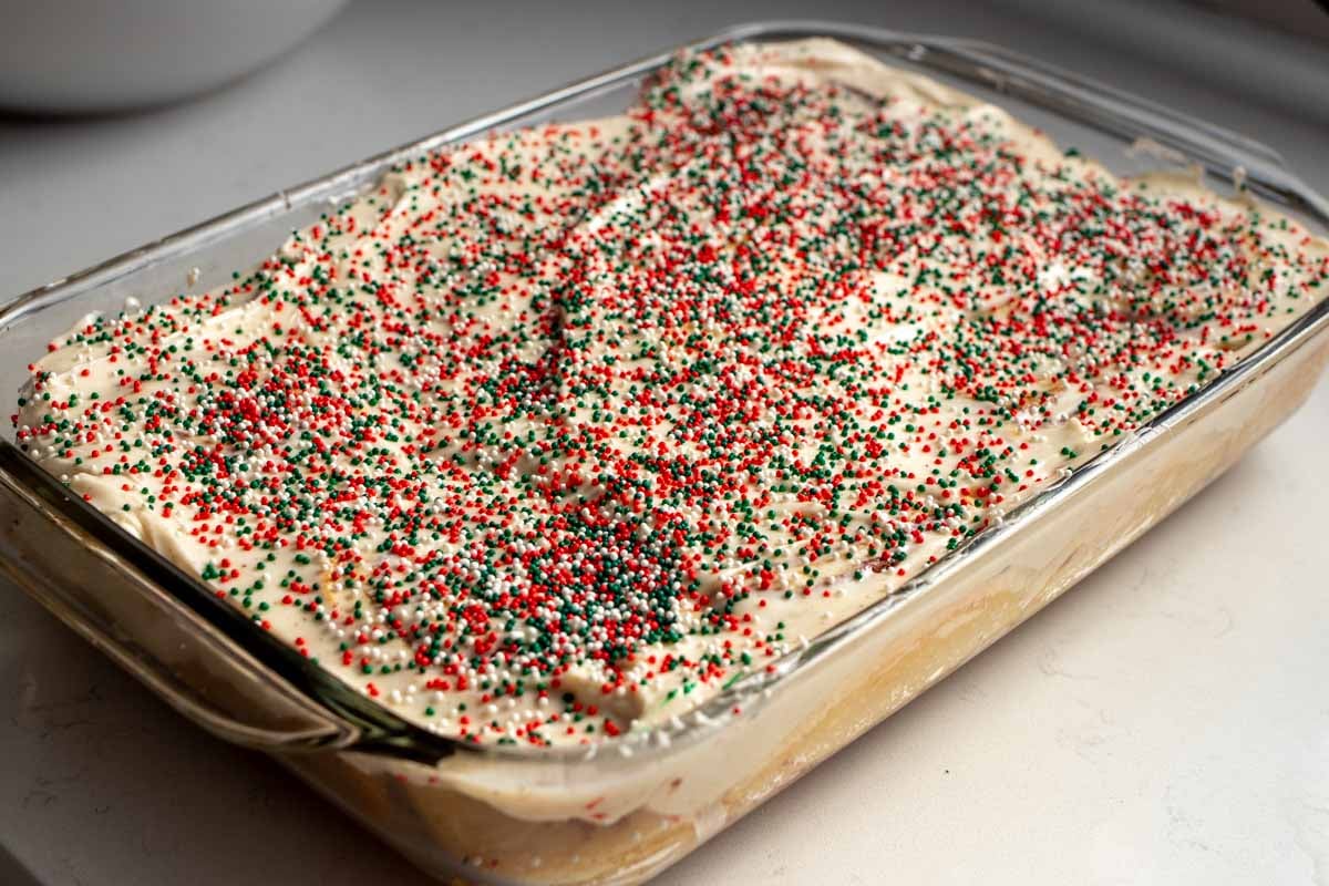 a big glass baking dish full of cinnamon rolls topped with sugar cookie icing and green and red sprinkles.