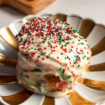 a single sugar cookie cinnamon roll on a gold and white christmas plate with green and red sprinkles for christmas.