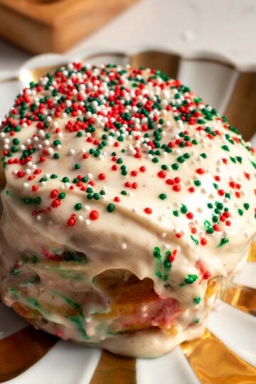 a single sugar cookie cinnamon roll on a gold and white christmas plate with green and red sprinkles for christmas.