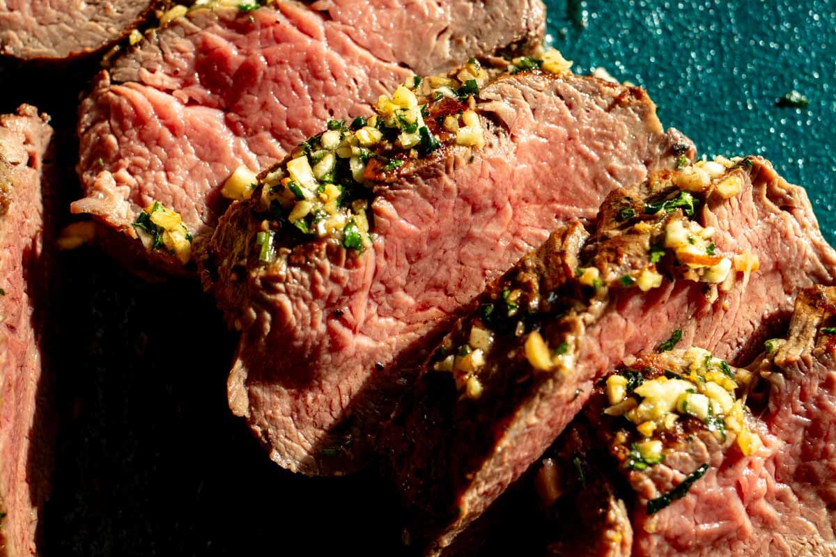 an up close view of a perfectly cooked whole beef tenderloin sliced into medallions.