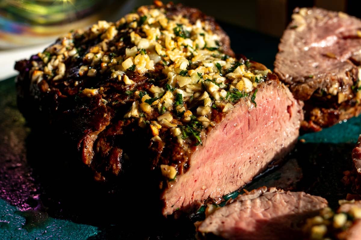 a beautifully cooked whole beef tenderloin topped with garlic butter and a beautiful pink medium rare center.