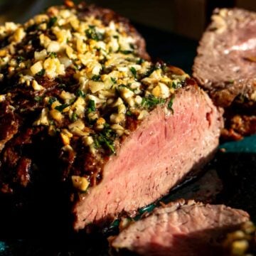 a beautifully cooked whole beef tenderloin topped with garlic butter and a beautiful pink medium rare center.