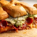 a pizza board topped with pepperoni pizza caesar salad sliders on kings hawaiian rolls..