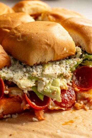 a pizza board topped with pepperoni pizza caesar salad sliders on kings hawaiian rolls..