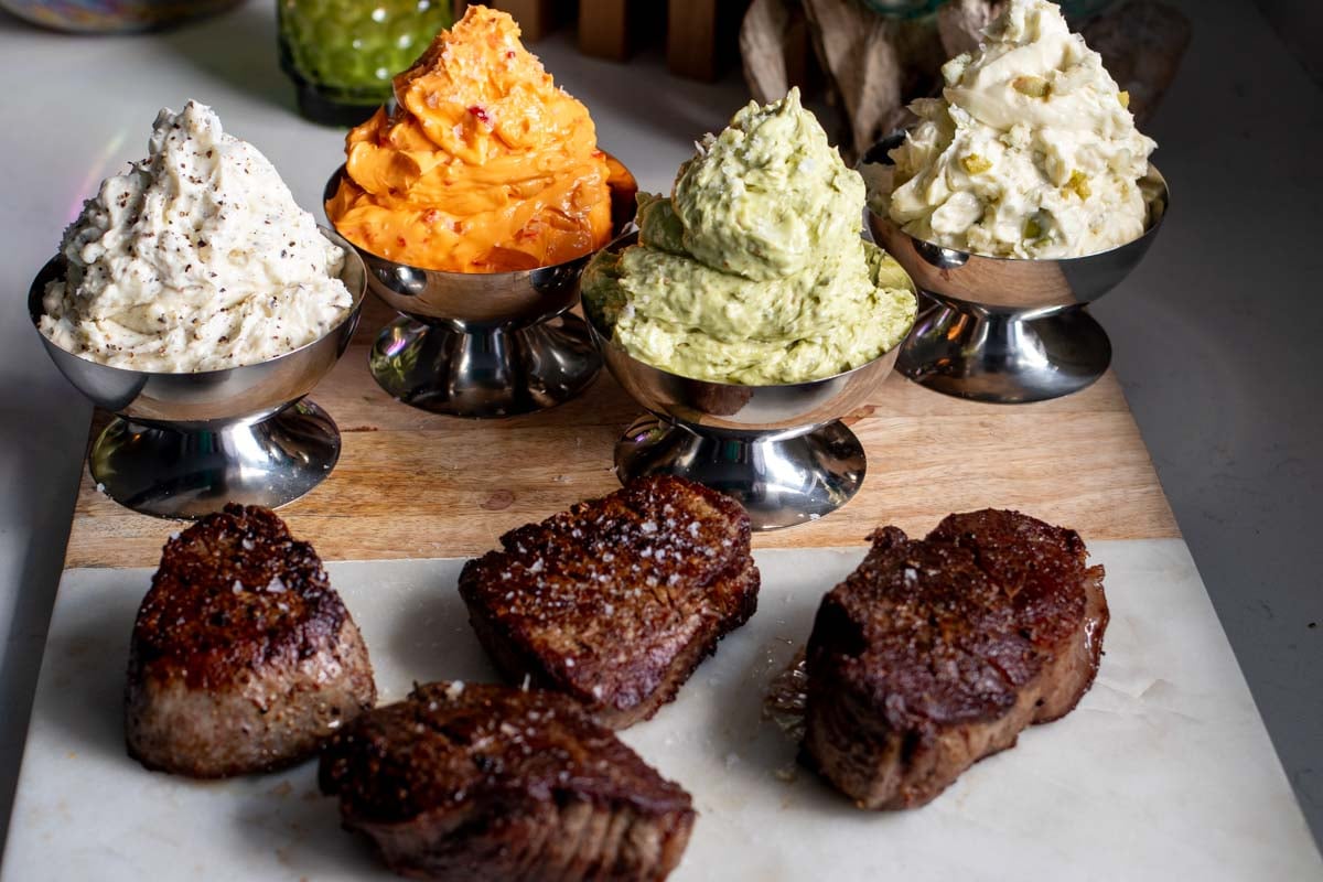 colorful compound butters in silver cups next to seared filet mignons.