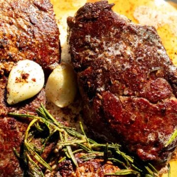 an up close look at some perfectly cooked filet mignons with green rosemary and garlic cloves.