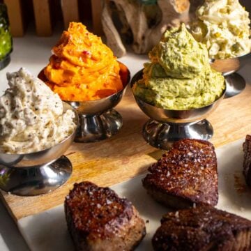 4 colorful compound butters for steak in silver cups with seared steaks on the side.
