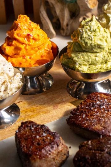 4 colorful compound butters for steak in silver cups with seared steaks on the side.