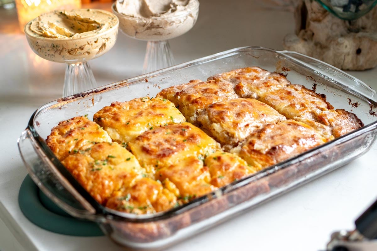 a glass baking dish full of butter swim biscuits with two flavored butters in the background.