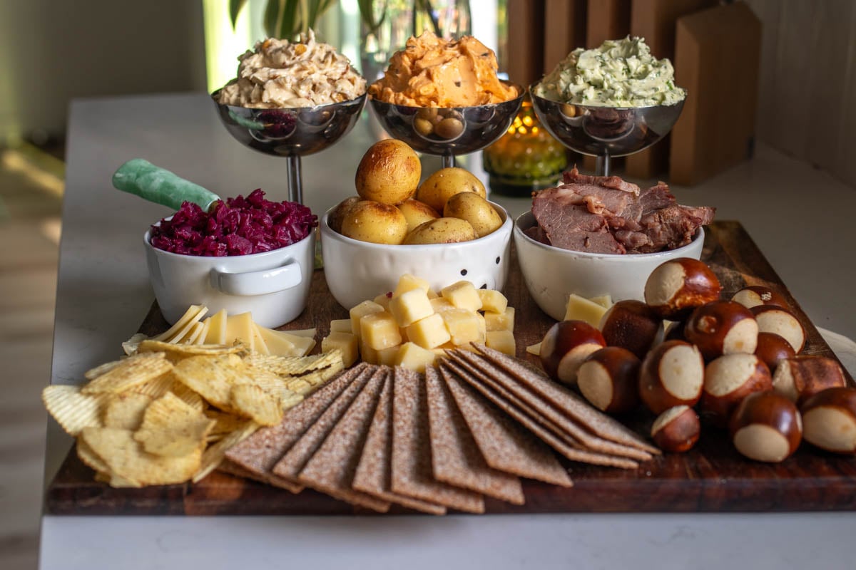 a st patricks day butter board on a white counter top with colorful bowls, flavored butters, and seasonal snacks.