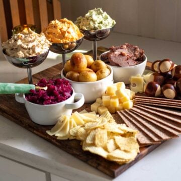 a st patricks day butter board on a white counter top with colorful bowls, flavored butters, and seasonal snacks.