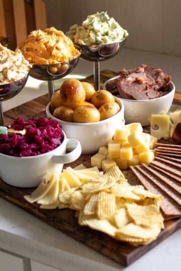 a st patricks day butter board on a white counter top with colorful bowls, flavored butters, and seasonal snacks.