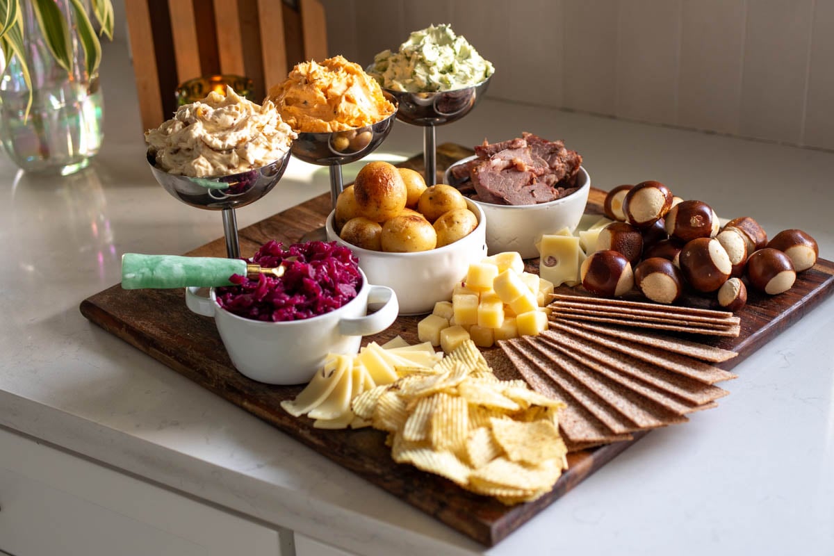 a st patricks day butter board on a white counter top with colorful bowls, flavored butters, and seasonal snacks.