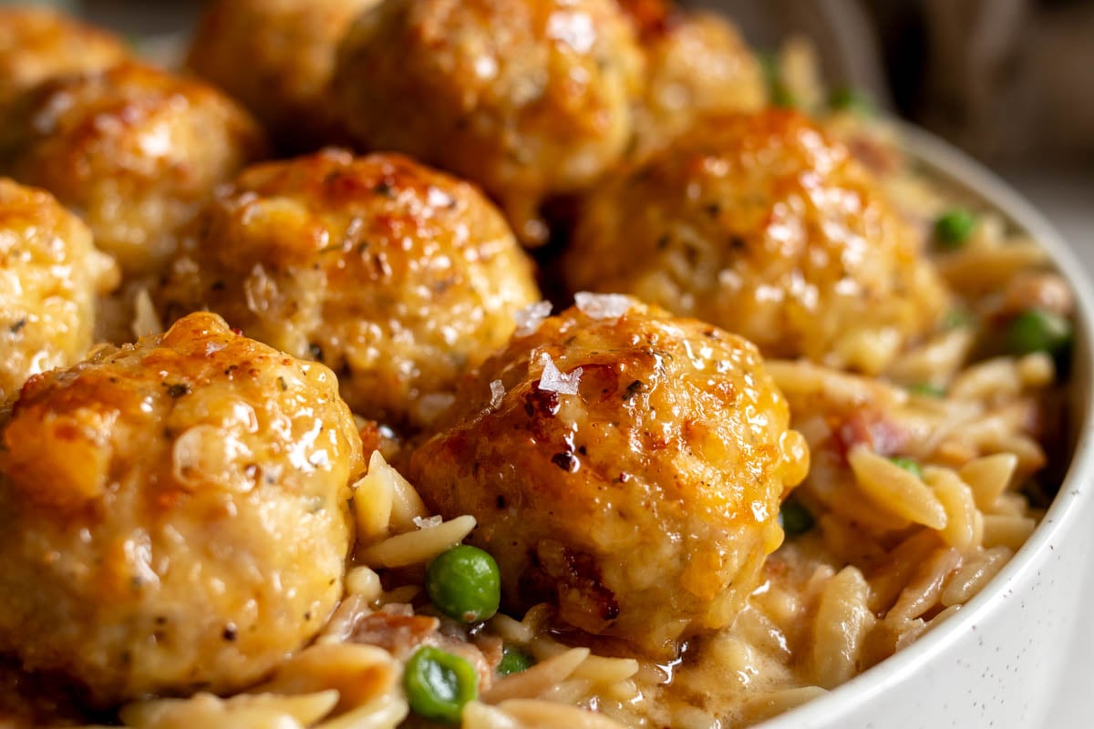 a bowl of cheesy baked chicken meatballs over creamy orzo.