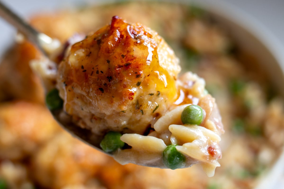 a spoon holding a baked chicken meatball over creamy pasta.