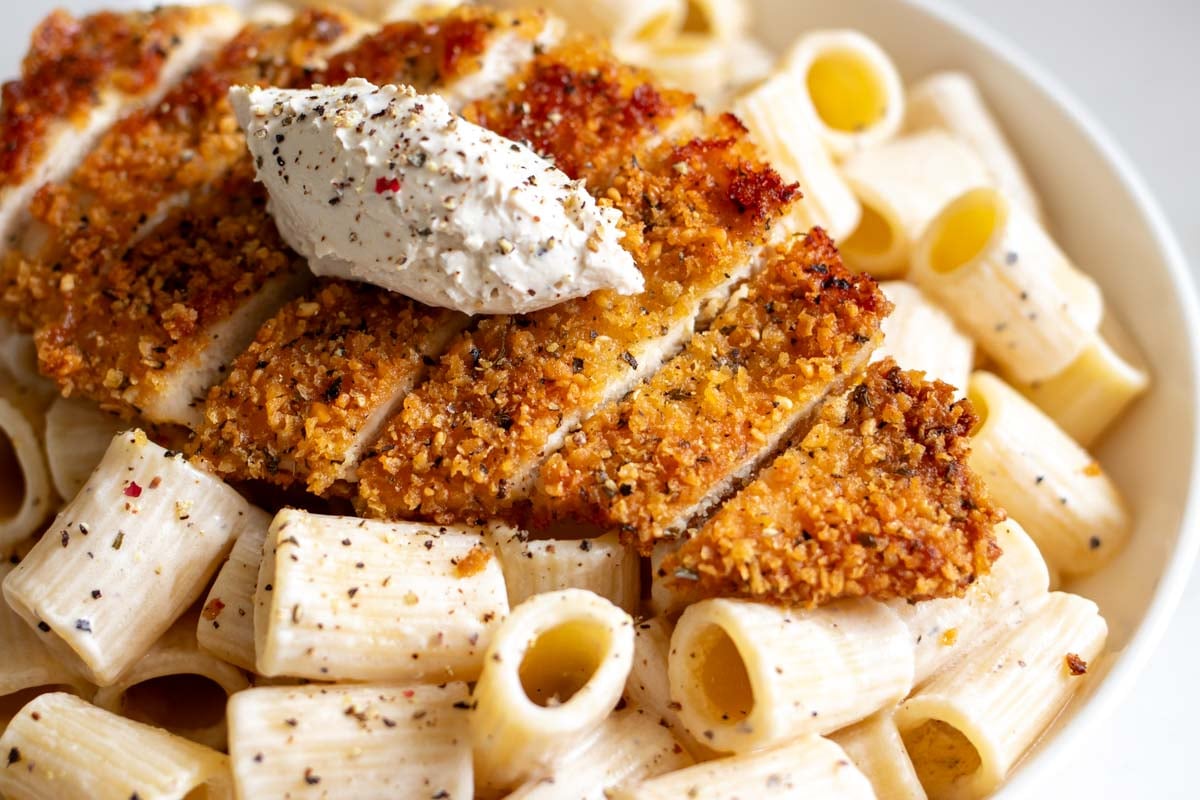 an up close view of a crispy chicken cutlet on top of creamy cacio e pepe pasta.