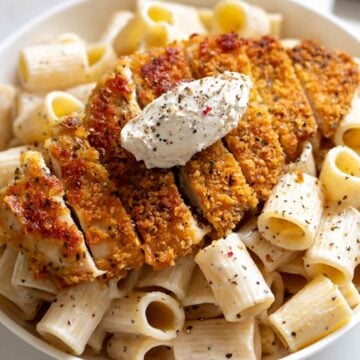 a crispy chicken cutlet with cacio e pepe pasta underneath all in a white bowl..