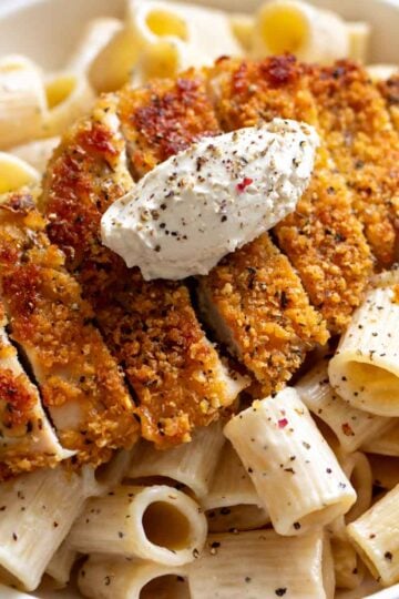 a crispy chicken cutlet with cacio e pepe pasta underneath all in a white bowl..