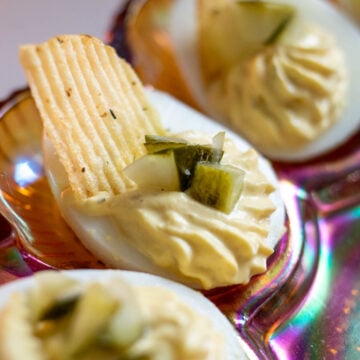 a close up of a dill pickled deviled egg with chopped dill pickles and a dill pickle potato chip on top.