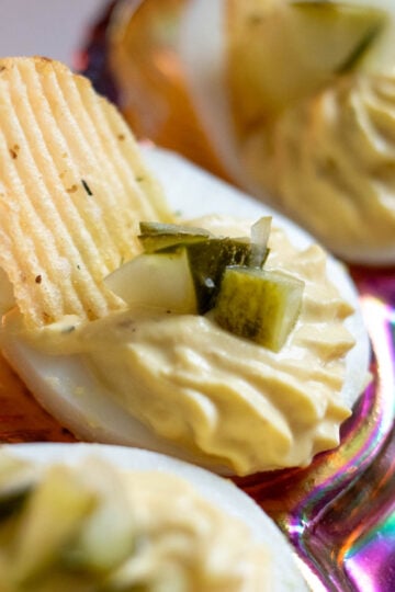 a close up of a dill pickled deviled egg with chopped dill pickles and a dill pickle potato chip on top.