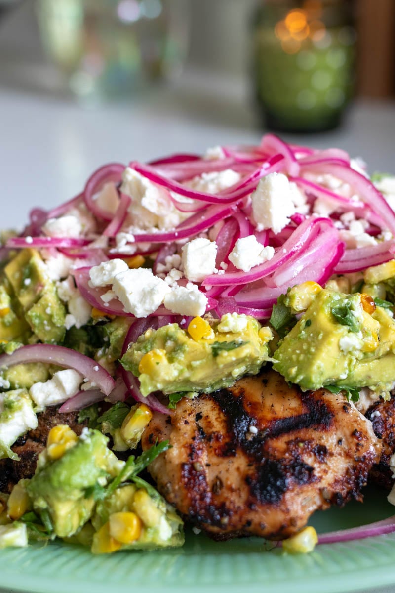 a green platter full of grilled chicken and a colorful salad on top.