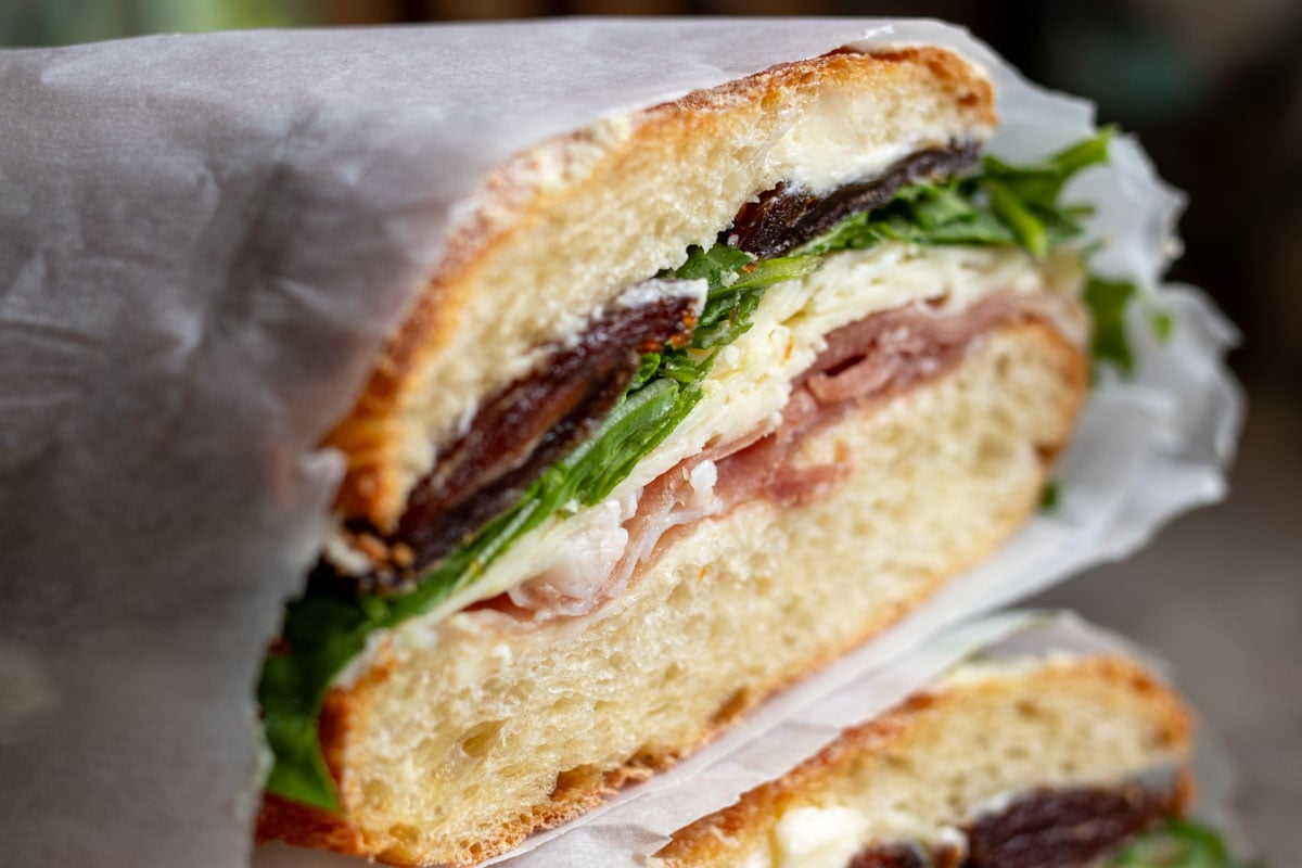 an up close look at the ingredients in this prosciutto butter sandwich with arugula, dates, cheddar, prosciutto, and french bread.