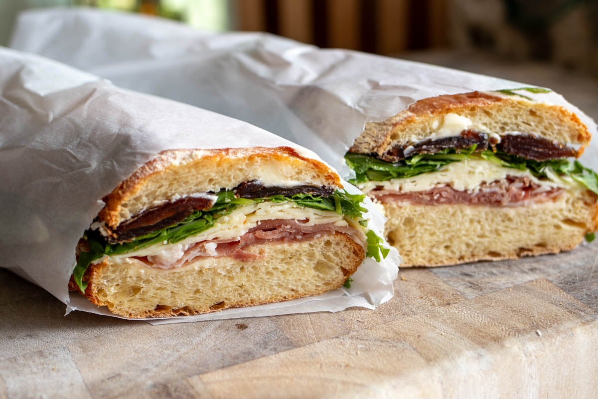 two halves of a prosciutto butter sandwich sitting on a cutting board.