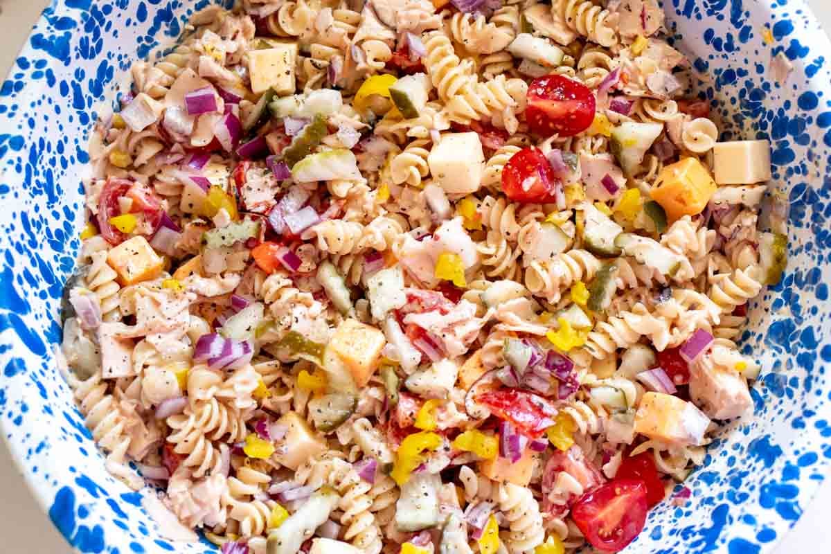 a big blue speckled crow canyon bowl with a bright and colorful pasta salad with bits of turkey and cheese in it. 