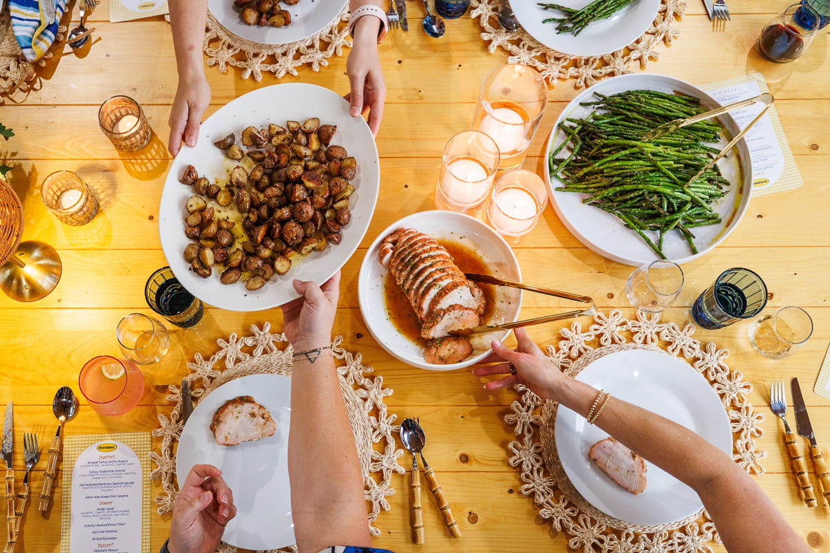hands and plates all helping serve each other on a large wooden dining table.