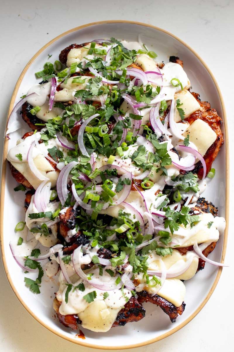 an overhead view of a white plate full of golden red bbq chicken topped with melted cheddar, onion, cilantro and scallions.